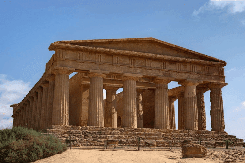 «Ο Ναός της Ομόνοιας στην Κοιλάδα των Ναών, Αγκριτζέντο, με τη χαρακτηριστική δωρική πρόσοψη και τους λαξευμένους κίονες κάτω από γαλανό ουρανό.»