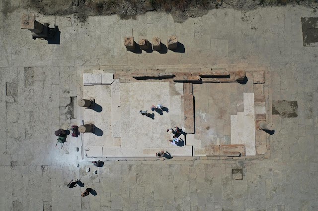 Εναέρια λήψη της μαρμάρινης αγοράς της αρχαίας Μαγνησίας, με διακριτά θεμέλια, κίονες και επισκέπτες να περιηγούνται στον αρχαιολογικό χώρο.