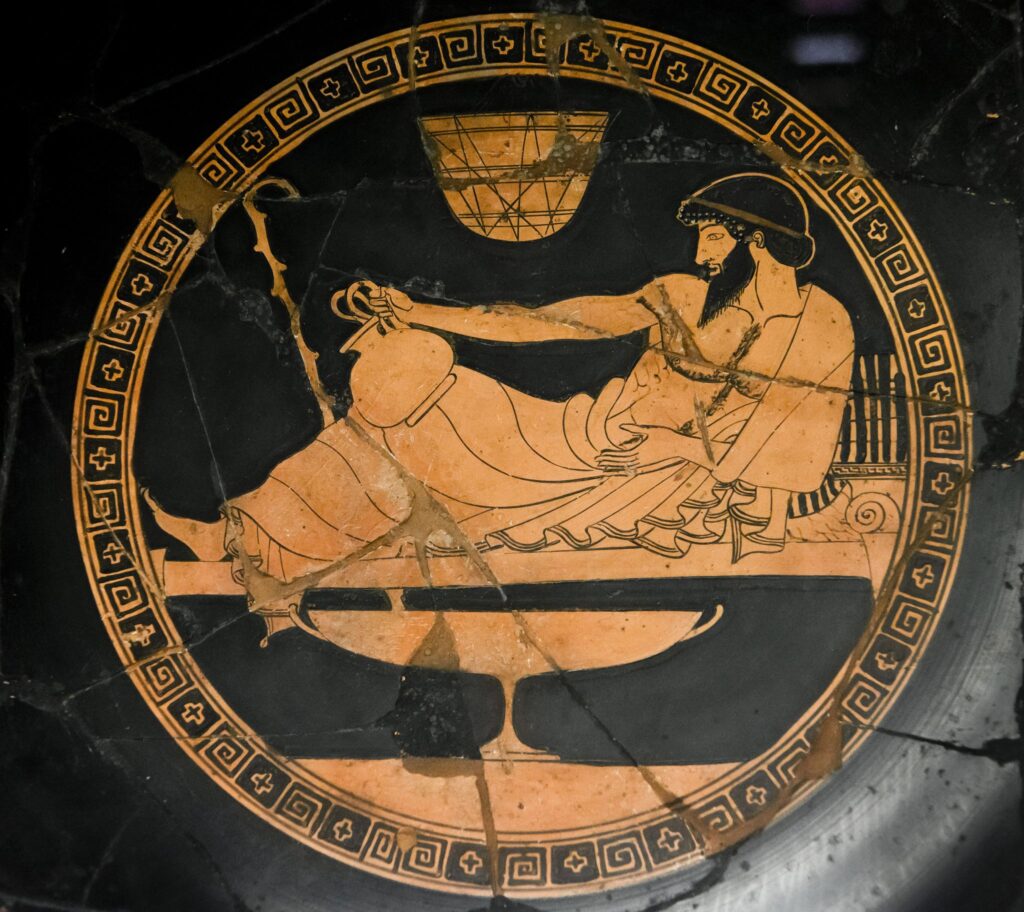 Αρχαίος Έλληνας ξαπλωμένος σε ανάκλιντρο, κρατώντας οινοχόη, σε ερυθρόμορφη αγγειογραφία.