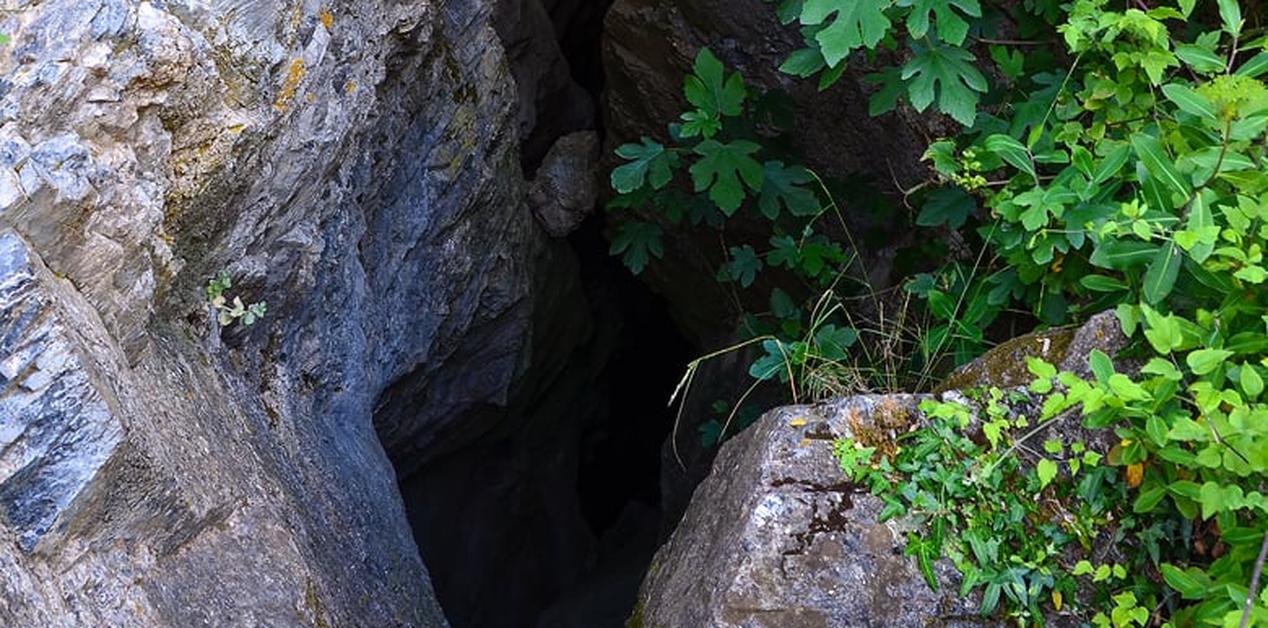 Είσοδος του φυσικού βάραθρου του Καιάδα στη Σπάρτη, περιτριγυρισμένη από βράχια και άγρια βλάστηση.