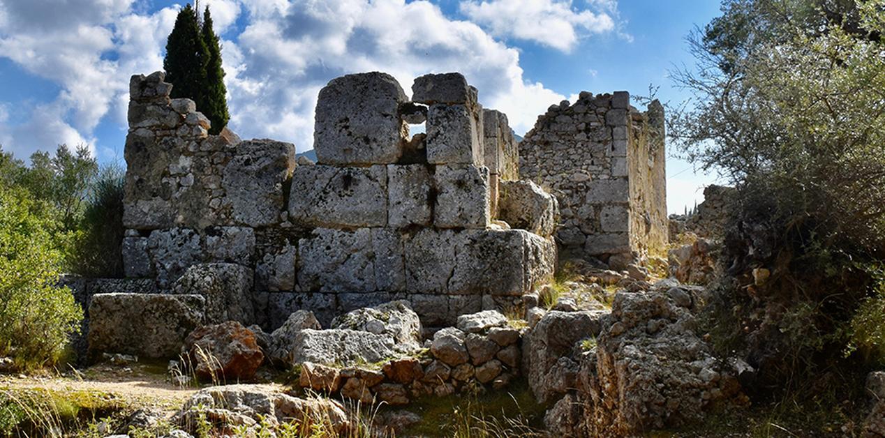 Ερείπια του αρχαίου Οδυσσείου στη Σχολή Ομήρου στην Ιθάκη, με μνημειακούς ογκόλιθους και τμήματα τοιχοποιίας κάτω από φωτεινό ουρανό.