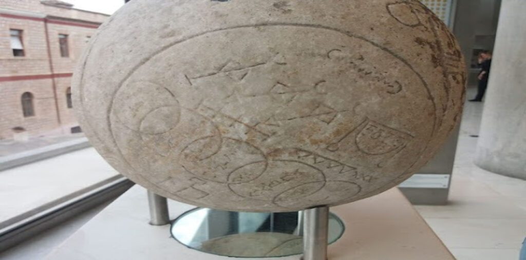 Κοντινό πλάνο σε τμήμα της Μαγικής Σφαίρας, που δείχνει λεπτομερώς τα σκαλισμένα γεωμετρικά σχήματα, όπως κύκλους, και τις γραμμικές μαγικές επιγραφές στην πέτρινη επιφάνειά της.