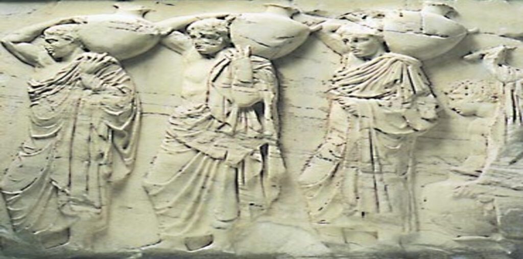 Κοντινή όψη μαρμάρινου ανάγλυφου από την αρχαία Ελλάδα. Τρεις ανδρικές μορφές με αρχαιοελληνικές ενδυμασίες βαδίζουν η μία πίσω από την άλλη, μεταφέροντας μεγάλες υδρίες στους ώμους τους, στο πλαίσιο πομπής.