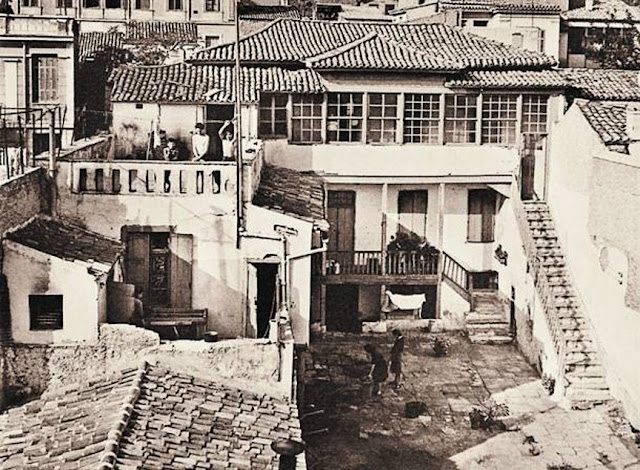 Ασπρόμαυρη φωτογραφία της οικίας Κοκοβίκου στην Πλάκα, δεκαετία 1950, αυλή με παραδοσιακά προσκτίσματα και ξύλινο χαγιάτι.