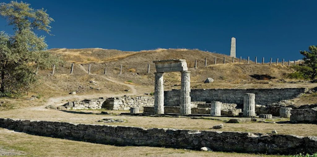 Τα ερείπια του Πρυτανείου της αρχαίας ελληνικής πόλης Παντικάπαιον, στην Κριμαία. Διακρίνονται οι πέτρινοι τοίχοι των θεμελίων και δύο πεσμένοι κίονες, με έναν οβελίσκο να δεσπόζει σε έναν λόφο στο βάθος.