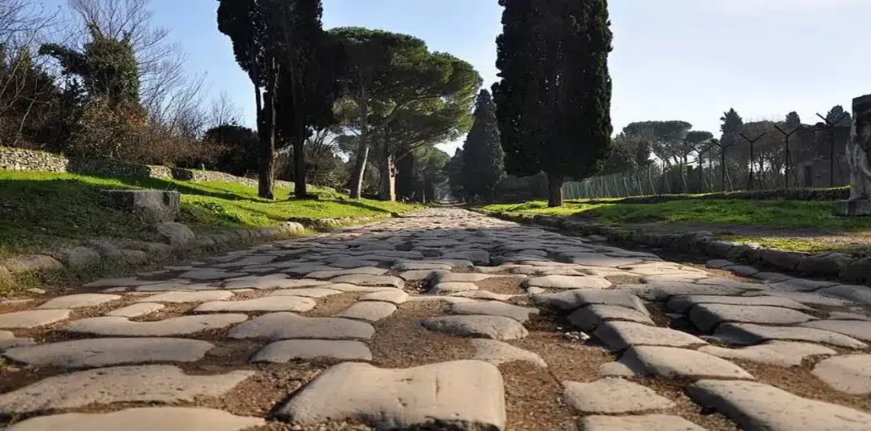 Λιθόστρωτος δρόμος της Via Appia Antica στη Ρώμη, με κυπαρίσσια και πεύκα να πλαισιώνουν το τοπίο