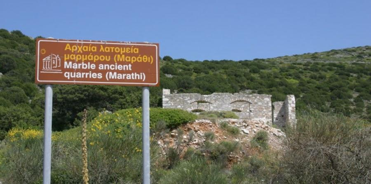 Αρχαία Λατομεία Μαρμάρου Πάρου (Μαράθι). Δείχνοντας προς ερείπια πέτρινου κτίσματος σε καταπράσινο λόφο κάτω από γαλανό ουρανό.