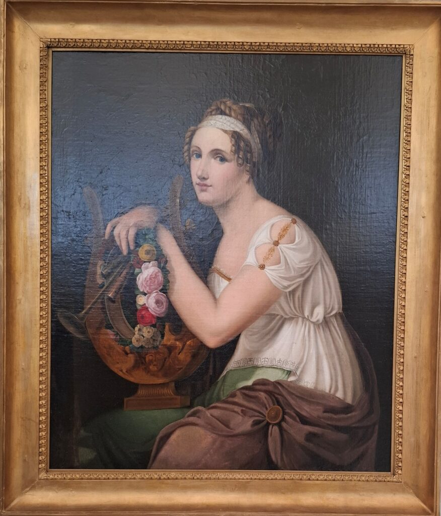 Κλασικός πίνακας ζωγραφικής της Μούσας Ευτέρπης, ντυμένης στα λευκά, η οποία ακουμπά σε μια λύρα στολισμένη με τριαντάφυλλα, μέσα σε χρυσή κορνίζα.