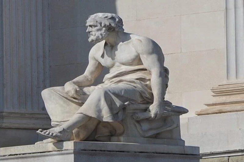 Όταν η δύναμη κερδίζει το δίκιο: Η αρχαία προειδοποίηση του Θουκυδίδη για το σήμερα - Μαρμάρινο άγαλμα του Θουκυδίδη σε εξωτερικό χώρο με φόντο κλασικούς κίονες. Ο ιστορικός κάθεται με χιτώνα και κρατάει πάπυρο, κοιτάζοντας προς το πλάι.