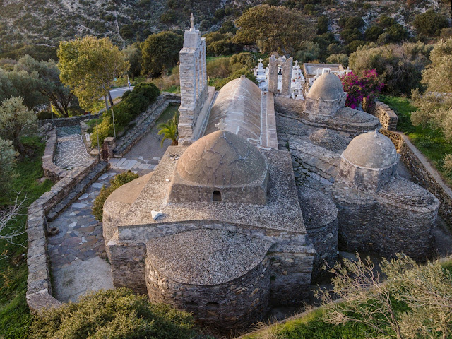 Πανοραμική λήψη της Παναγίας Δροσιανής στη Νάξο, ένας λίθινος βυζαντινός ναός με πολλαπλούς τρούλους και ιδιόμορφη αρχιτεκτονική, περιτριγυρισμένος από ελαιώνες.