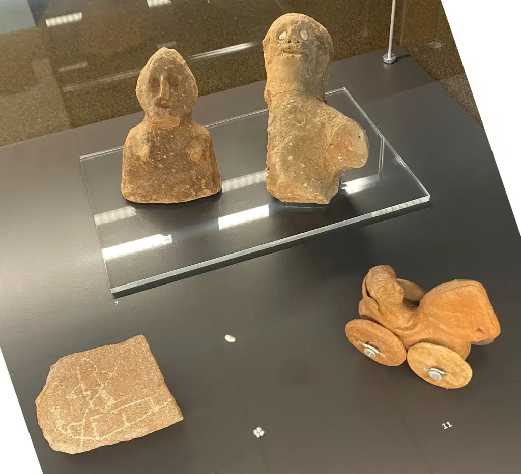 Αρχαία πήλινα αντικείμενα: δύο ανθρωπόμορφα ειδώλια, ένα θραύσμα με εγχάρακτο σχέδιο και ένα παιδικό παιχνίδι με ρόδες.