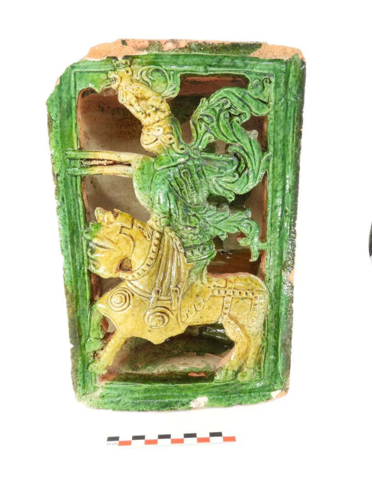 Ένα ορθογώνιο κεραμικό πλακίδιο σόμπας με πράσινο υάλωμα, που φέρει ανάγλυφη παράσταση ενός έφιππου άνδρα.