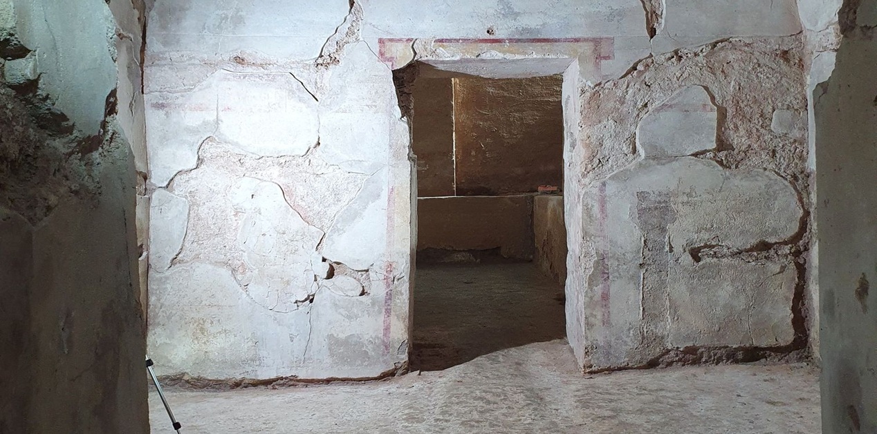 Εσωτερική άποψη αρχαίου Μακεδονικού τάφου στη Δράμα. Διακρίνεται ο προθάλαμος με το πέρασμα προς τον κυρίως θάλαμο, οι φθαρμένοι σοβάδες στους τοίχους και τα ίχνη κόκκινης γραμμικής διακόσμησης γύρω από το άνοιγμα της θύρας.