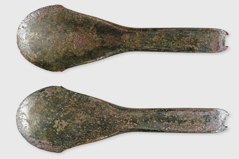 Δύο όψεις ενός αρχαίου χάλκινου τσεκουριού σε λευκό φόντο.