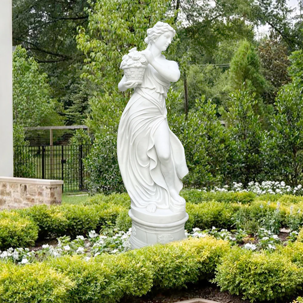 Μαρμάρινο άγαλμα αρχαιοελληνικής θεάς, ίσως της Δήμητρας, σε έναν κήπο, κρατώντας ένα καλάθι με φρούτα και λουλούδια, σύμβολο του θηλυκού στοιχείου και της σύνδεσης με τη φύση.