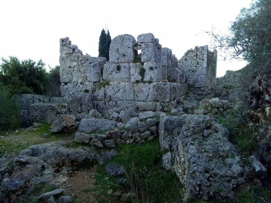 Αρχαία πέτρινα ερείπια με κυκλώπεια τείχη σε κατάφυτο περιβάλλον, στην τοποθεσία Σχολή του Ομήρου στην Ιθάκη.