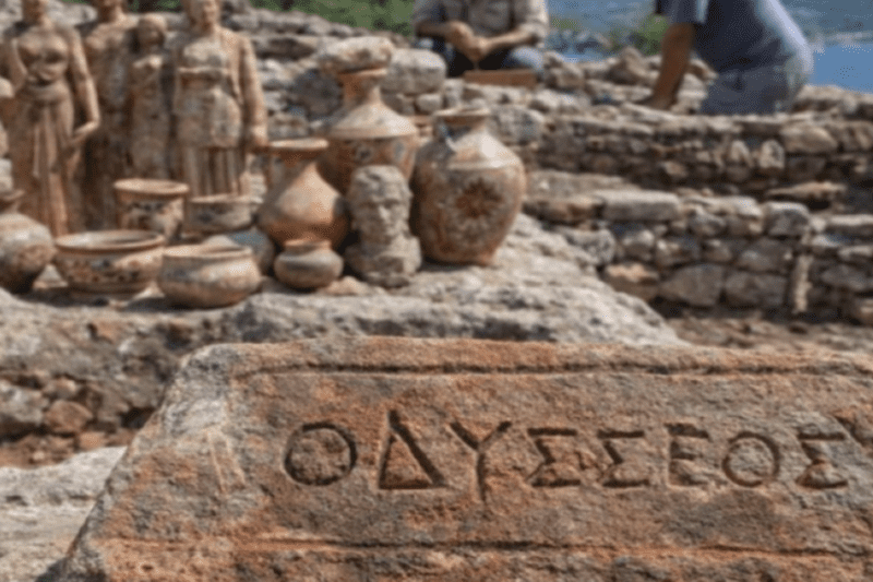 Πέτρα με σκαλισμένη τη λέξη "ΟΔΥΣΣΕΟΣ" σε πρώτο πλάνο, με φόντο αρχαιολογικά ευρήματα και εργάτες σε ανασκαφή.
