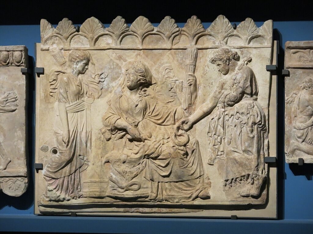 Ανάγλυφη πλάκα σε τερακότα που δείχνει μια καθισμένη θεά, πιθανόν τη Δήμητρα, με μια ιέρεια που προσφέρει στάχυα και μια άλλη γυναίκα με δάδα.