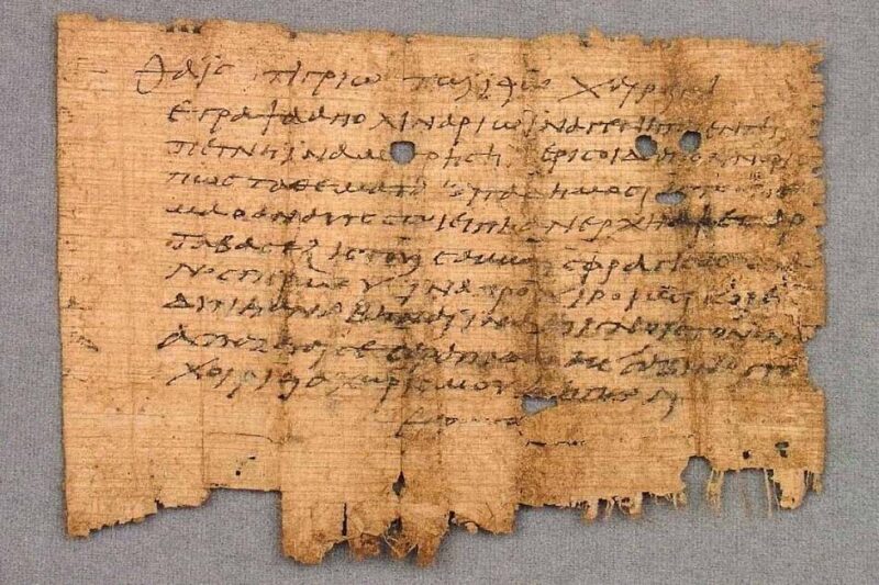 Φθαρμένο κομμάτι αρχαίου παπύρου με ελληνικό κείμενο σε επισεσυρμένη γραφή.