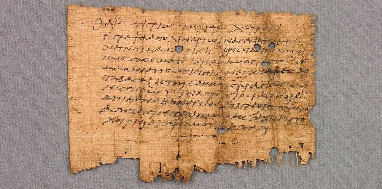 Φθαρμένο κομμάτι αρχαίου παπύρου με ελληνικό κείμενο σε επισεσυρμένη γραφή.