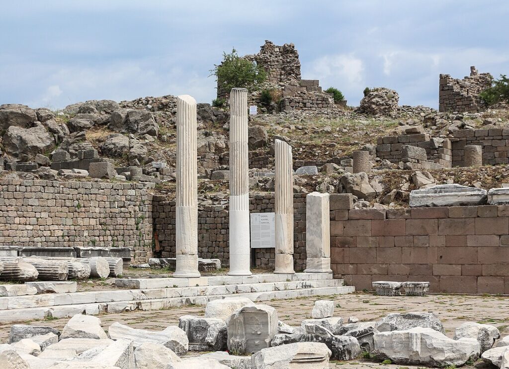 Αρχαιολογικός χώρος Περγάμου με τρεις όρθιους κίονες και ερείπια οχύρωσης στο βάθος.