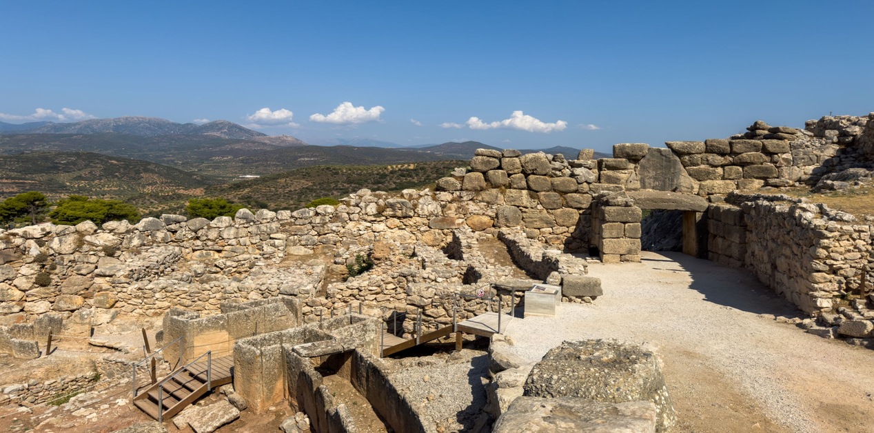 Τα επιβλητικά Κυκλώπεια τείχη σε αρχαιολογικό χώρο της Πελοποννήσου κάτω από γαλάζιο ουρανό.
