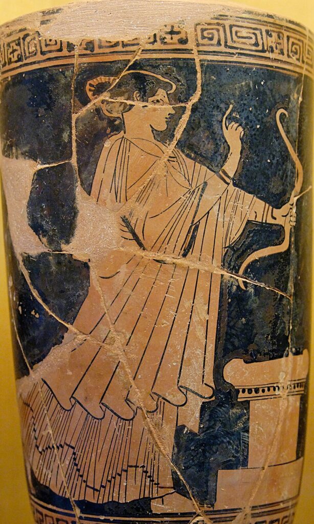 Θραύσμα αρχαίου ελληνικού αγγείου που δείχνει μια γυναίκα με μακρύ φόρεμα να κρατά ένα κυρτό τόξο δίπλα σε μια κολόνα.