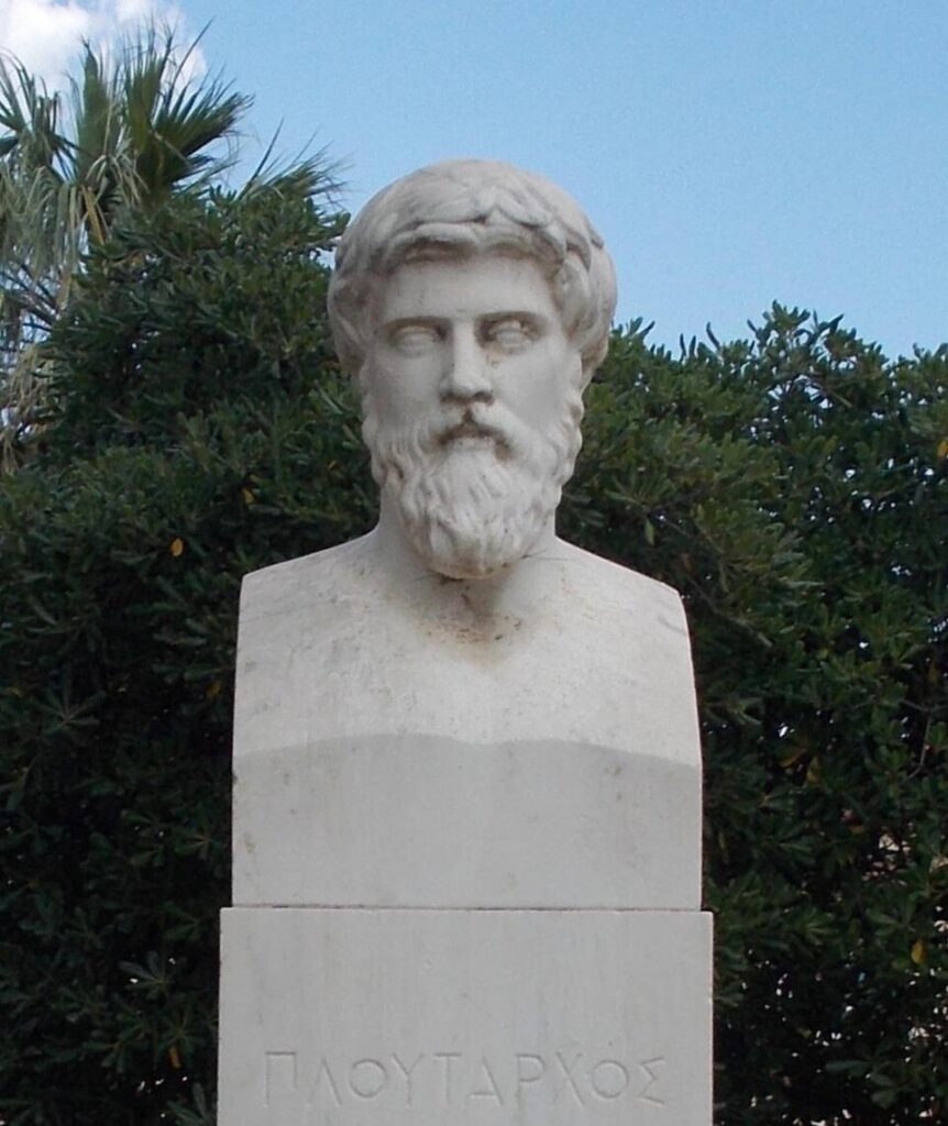 Κλασική μαρμάρινη προτομή του φιλοσόφου Πλούταρχου σε εξωτερικό χώρο με φόντο πράσινη βλάστηση.