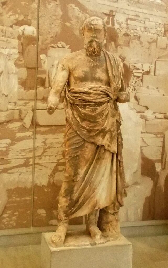 Αρχαίο μαρμάρινο άγαλμα του Πλούταρχου με ιμάτιο που εκτίθεται σε αρχαιολογικό μουσείο.
